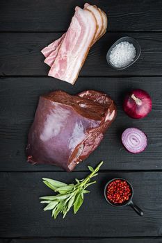 Beef liver with bacon and onion on black wooden background, top view.