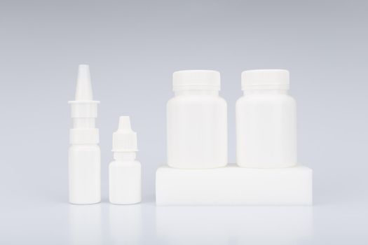Simple still life with nose spray, eye drops and two white unbranded medication bottles on podium against light grey background. High quality photo