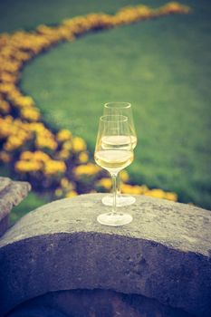 Glass of white wine on a stone wall in the formal garden. Enjoying it in the own garden in the evening sun.