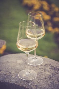 Glass of white wine on a stone wall in the formal garden. Enjoying it in the own garden in the evening sun.