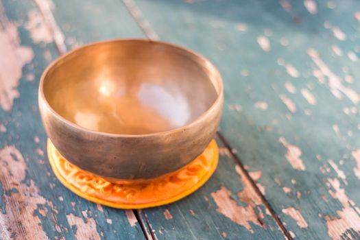 Metal singing bowl on a rustic green, wooden table outdoors. Flowers in the colourful, blurry background