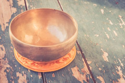 Metal singing bowl on a rustic green, wooden table outdoors. Flowers in the colourful, blurry background