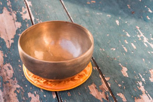 Metal singing bowl on a rustic green, wooden table outdoors. Flowers in the colourful, blurry background