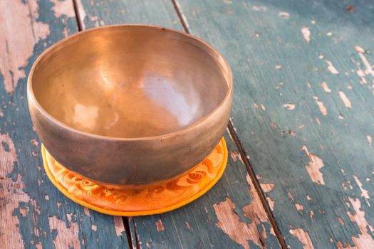 Metal singing bowl on a rustic green, wooden table outdoors. Flowers in the colourful, blurry background