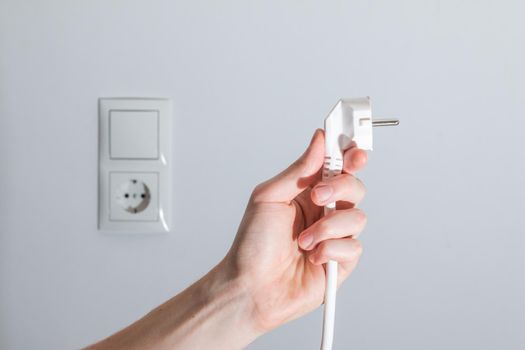 White plug with cable in males hand, ready to connect. Energy concept.