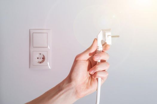 White plug with cable in males hand, ready to connect. Energy concept.