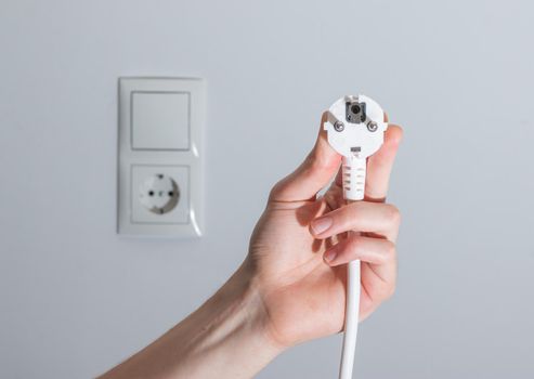 White plug with cable in males hand, ready to connect. Energy concept.