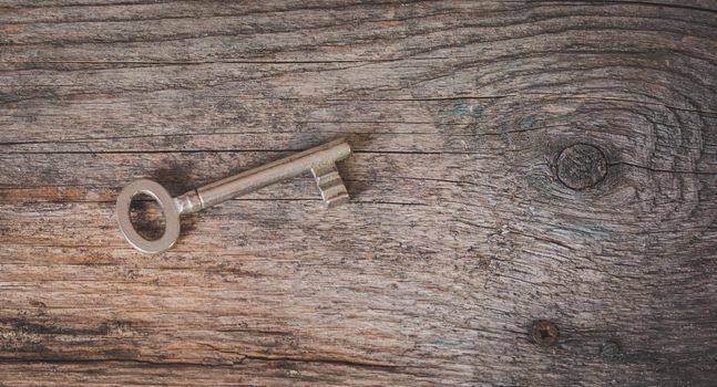 Old key is lying on a rustic wooden desk