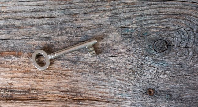 Old key is lying on a rustic wooden desk