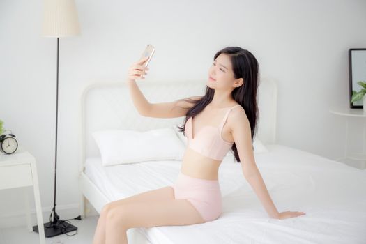 Beautiful young asian woman sexy in underwear talking a selfie on smartphone for social network in the bedroom, girl in lingerie relax with taking a picture on mobile phone on bed in the bedchamber.