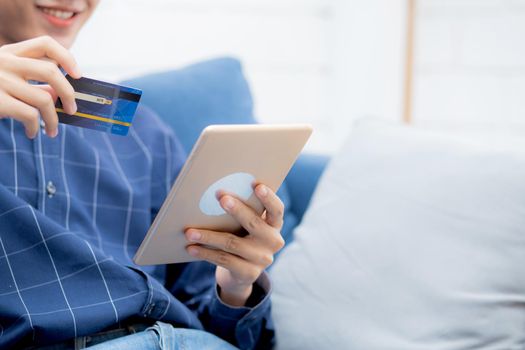 Young asian man smiling holding credit card shopping online with tablet computer buying and payment, male using debit card purchase or transaction of finance, lifestyle and e-commerce concept.