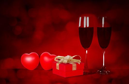 Two wineglasses and red gift box and heart shape on desk with red blur bokeh background, champagne glasses and presents with celebration and anniversary, love and romantic, valentine day concept.