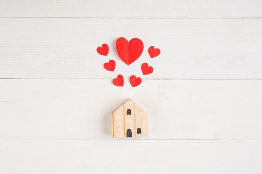 Wood house with heart shape paper on white wooden desk background, love and harmony of family, residence and insurance, symbol and sign, top view, flat lay, copyspace, nobody.