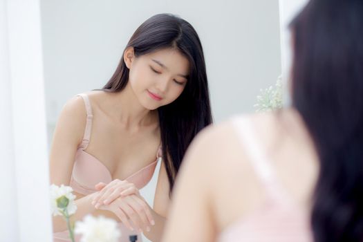 Beautiful sexy young asian woman looking mirror applying cream on hand and message, beauty girl applying body lotion skin care for health and soft hydration, treatment and cosmetic with moisturizer.