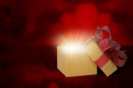 Gold gift box with ribbon open and light blurred bokeh background, present with luxury for love and anniversary with glowing and sparkle in festive, copy space, Valentine day or Christmas concept.