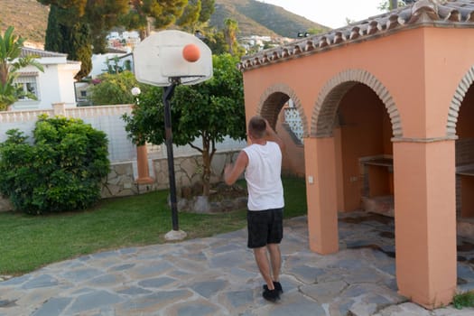 Young man plays basketball throws a ball into a basket in a jump
