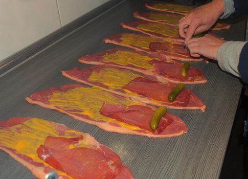 Preparation of fresh beef roulades, raw meat coated with mustard and onions.