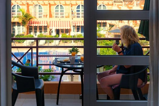 Woman having breakfast and brunch on the balcony of a luxury hotel restaurant and eating. Overlooking the pool.