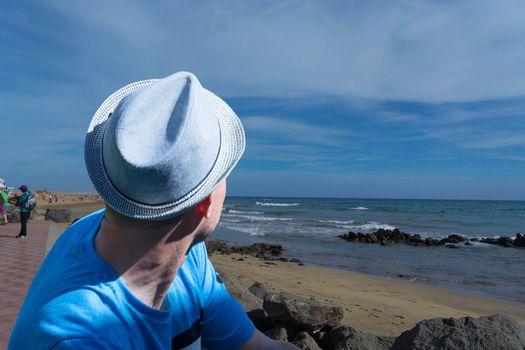 Man sits on rocks on the beach and enjoys the view. Summer concept.