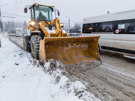 TULA, RUSSIA - NOVEMBER 21, 2020: Yellow tractor with large scoop cleaning snow on road at winter day light.