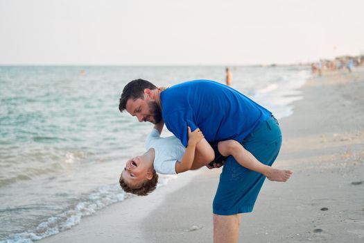 Father son spending time together sea vacation Young dad child little boy walking beach Fathers day. Family with one child. Happy childhood with daddy. sitting on hands laughs