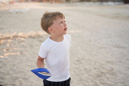 Caucasian boy standing beach. Childhood summertime. Family vacation with one child. Handsome little kid with toy handmade ship