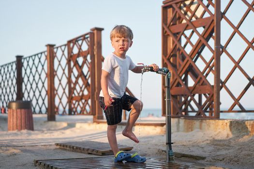 Child wash legs after beach sand Caucasian boy standing beach. Childhood summertime. Family vacation with one child.