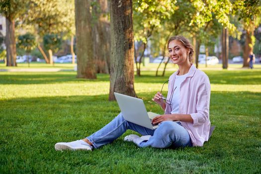 Businesswoman sitting grass summer park using laptop Business person working remote. Outdoor Successful european caucasian woman freelancer make video call teacher study work online lessons