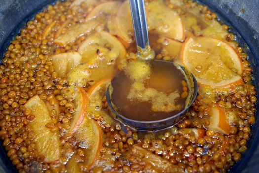 closeup of mulled wine citrus fruit, preparing in big old metal kettle on fire, above view, Traditional Christmas fair market beverage