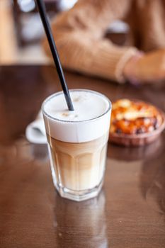 Hot Latte coffee in a glass and a fresh apple dessert next to it. The hot drink is served with a plastic straw. Delicious breakfast in the cafe