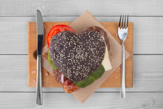 Heart shape love black hamburger, burger fast food concept, Valentines day surprise dinner, wooden background, top view flat lay