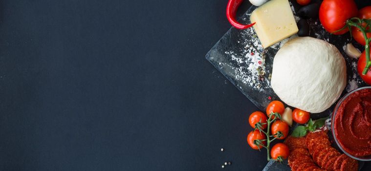 Raw dough for pizza with ingredients and spices on black table background with copy space for text