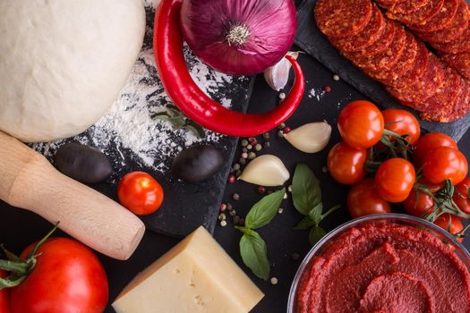 Raw dough for pizza with ingredients and spices on black table background