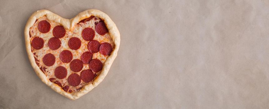 Pizza heart shaped with pepperoni on craft brown paper background. Concept of romantic love for Valentines Day . Love food, Copy space for text
