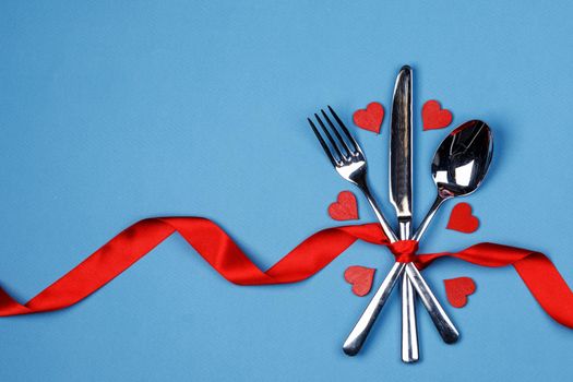 Cutlery set tied with red silk ribbon and hearts on blue background Valentine day dinner concept