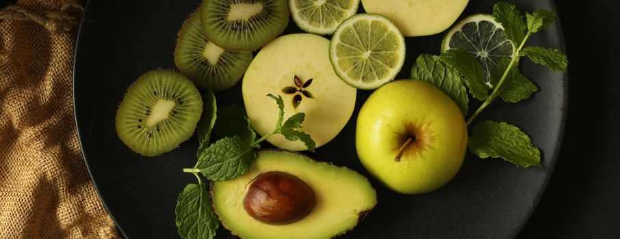 Healthy green fruit background. Green fruits, apples. kiwi, lemon, mint on black plate with canvas bag. Horizontal flat lay, above view