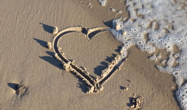 A beautiful heart shape painted into the sand of a baltic sea beach with some water waves