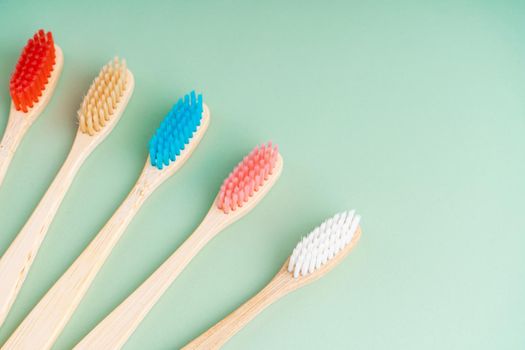 A set of Eco-friendly antibacterial toothbrushes made of bamboo wood on a light green background. Environmental care trends.