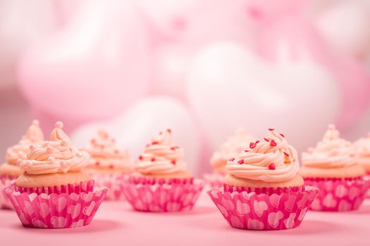 Valentine day love cupcakes decorated with cream and hearts on pink and white party balloons background with copy space for text
