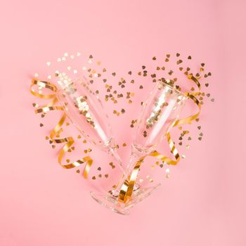 Valentines day champagne flutes glasses and heart shaped golden glitters on pink background with copy space for text