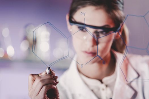 Portrait of a confident female health care expert in life science laboratory writing structural chemical formula on a glass board. Healthcare and modern life science concept. Blue toned image.