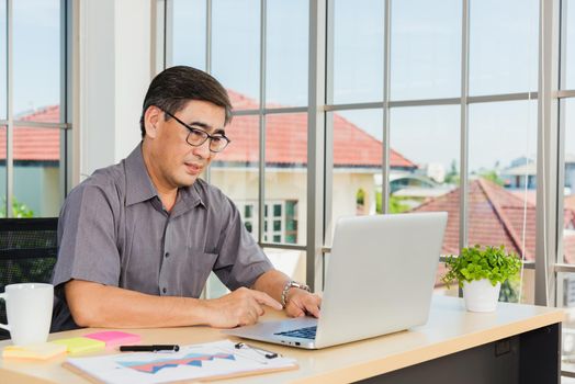 Asian senior business man working online on a modern laptop computer he looking at the screen for remote online studying. Old businessman people using the laptop to video call conference on desk table