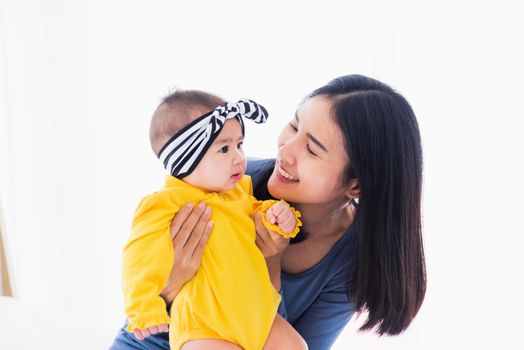 Portrait of beautiful young Asian mother playing and smiling together with his newborn little baby at home, Parent mom and little kid relaxing in the bedroom, Family having fun together