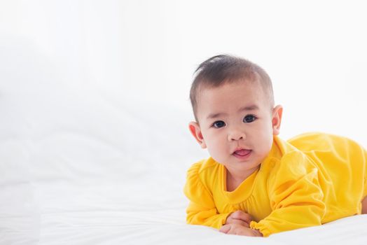 Portrait of beautiful young Asian newborn little baby prone on the bed at home, Happy baby smile wears a yellow shirt relaxing in the room, Family morning at home