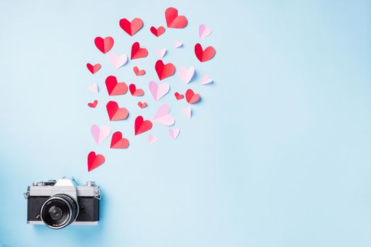 Valentines' day background. Vintage retro camera and paper flying elements hearts cut greeting gift card on blue background, Symbol of love. Happy Valentines Day and I love photography concept