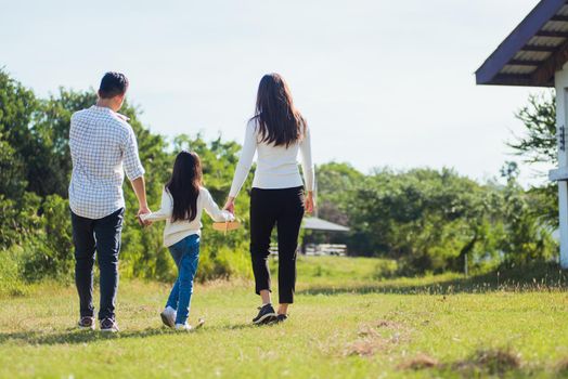 Happy Asian young family father, mother and child little girl having fun and enjoying outdoor walking down the road outside together in green nature park on a sunny summer day