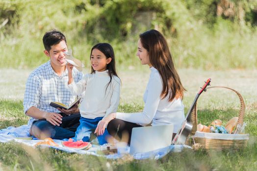 Happy Asian young family father, mother and child little girl having fun and enjoying outdoor sitting on picnic blanket playing toy aircraft at summer garden park