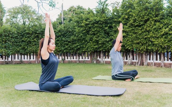 Asian man and woman practicing doing yoga outdoors in meditate pose sitting on green grass. Young couple stretching in nature a field garden park. Meditation, exercise health care concept