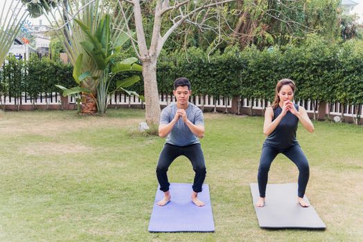 Asian man and woman practicing doing yoga outdoors in meditate pose stand on green grass. Young couple stretching in nature a field garden park. Meditation, exercise health care concept