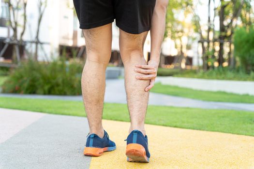 Male runner athlete leg injury and pain. Hands grab painful leg while running in the park.